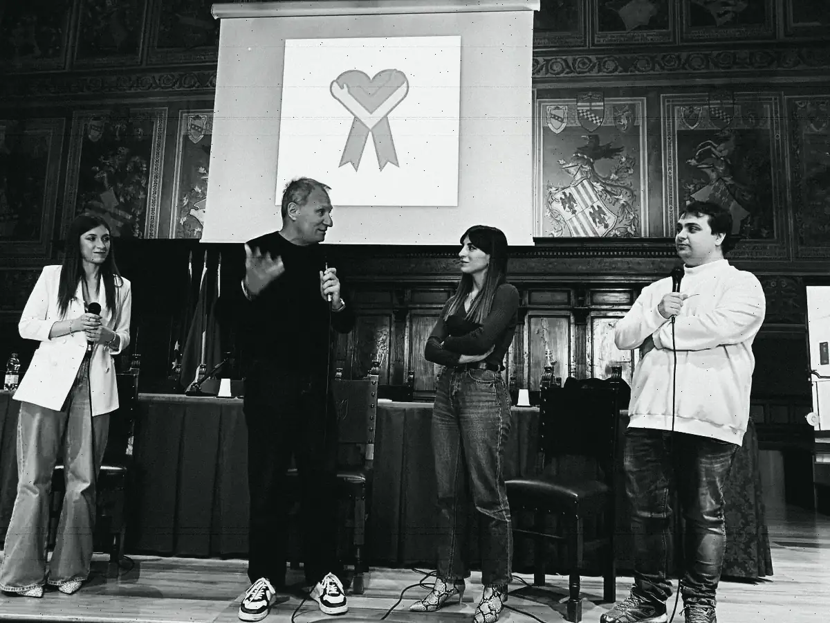 Il palco del Palazzo dei Notari: quattro relatori in piedi coi microfoni sotto il logo di Corabea proiettato