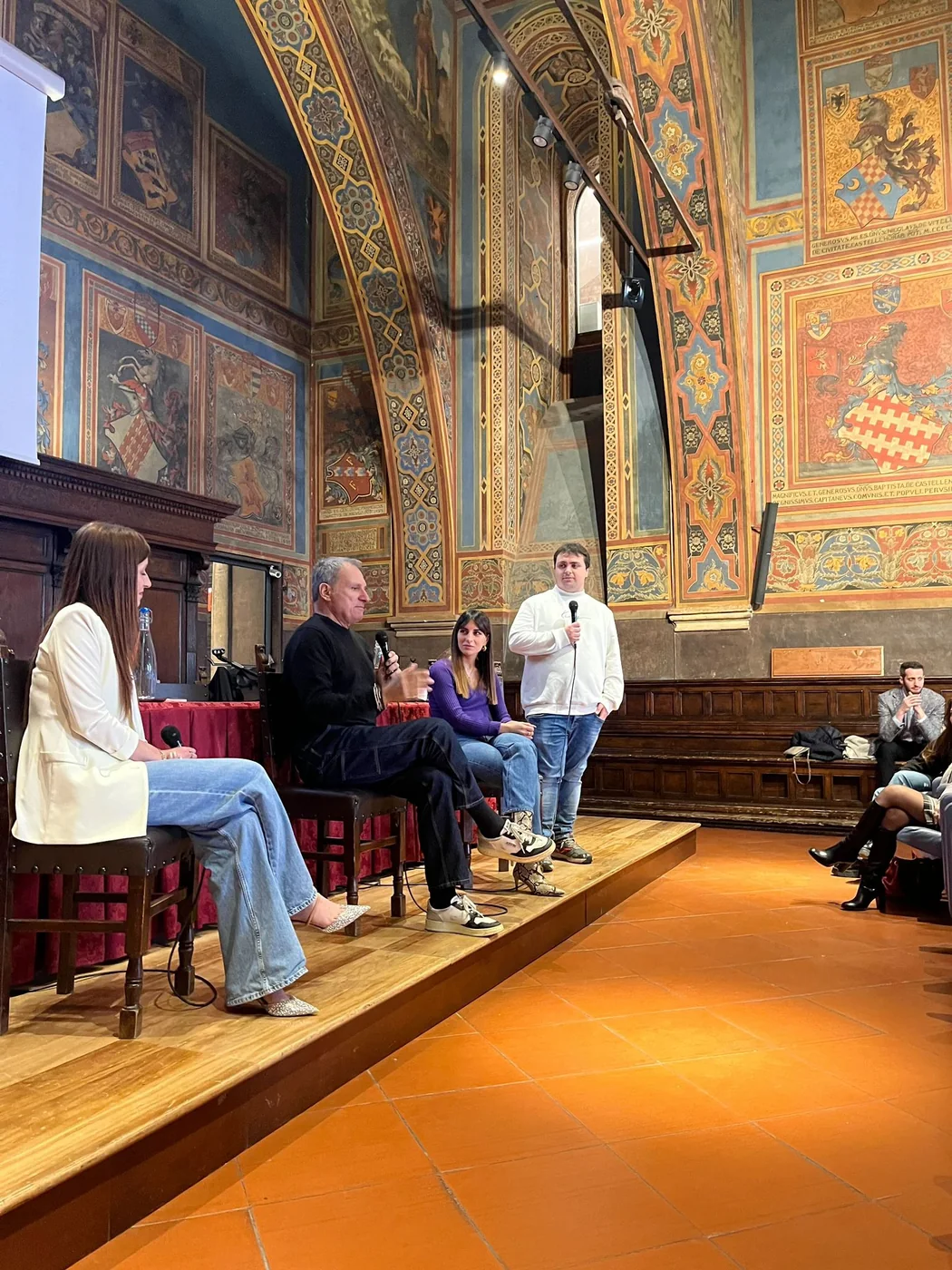 Il panel della presentazione di Corabea sotto gli affreschi del Palazzo dei Notari: Francesco in piedi con il microfono accanto ai relatori seduti