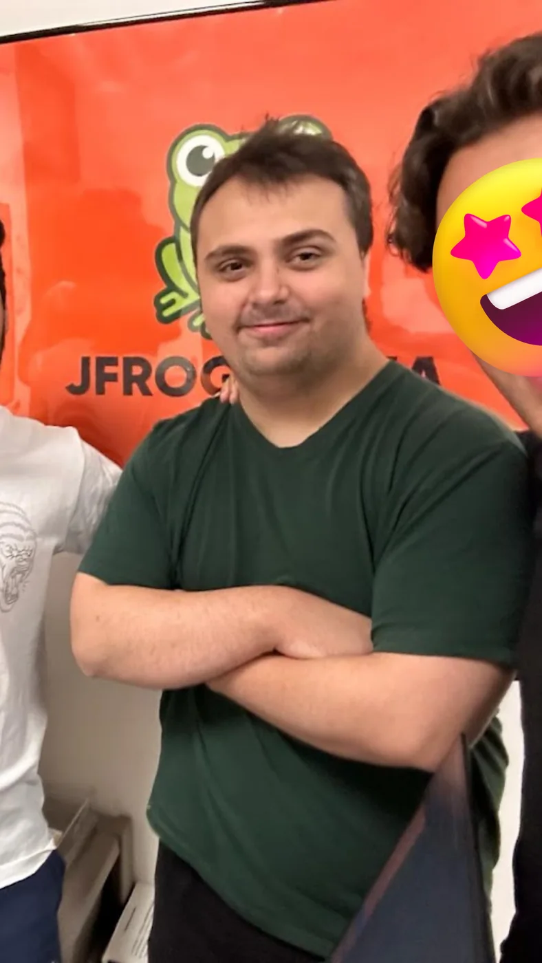 Francesco a braccia conserte davanti al banner arancione di JFrog Media, con due colleghi